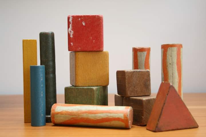 Red, yellow, brown, green, blue and orange toy wooden building blocks arranged in towers. Shapes include cubes, cylinders and a triangle